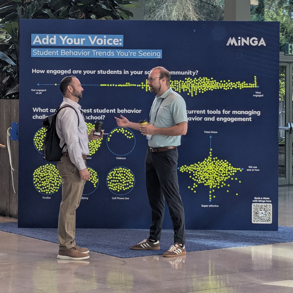 A Minga team member talks with an educator in front of Minga's Engagement Wall at the UNITED 2025 Conference in Seattle.